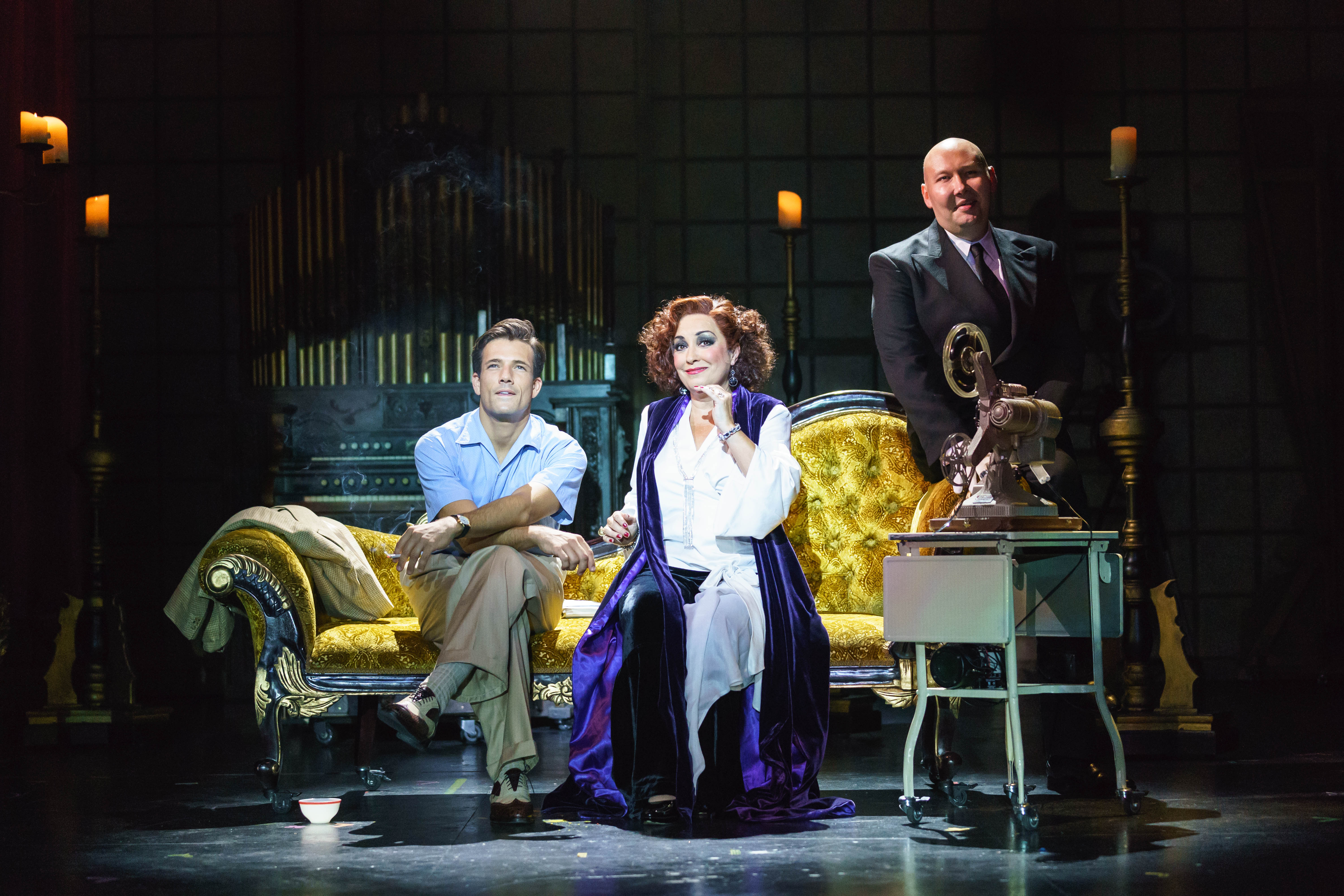 An image from Sunset Boulevard of Danny Mac, Ria Jones sitting on a sofa starring into the distance with Adam Pearce standing close by