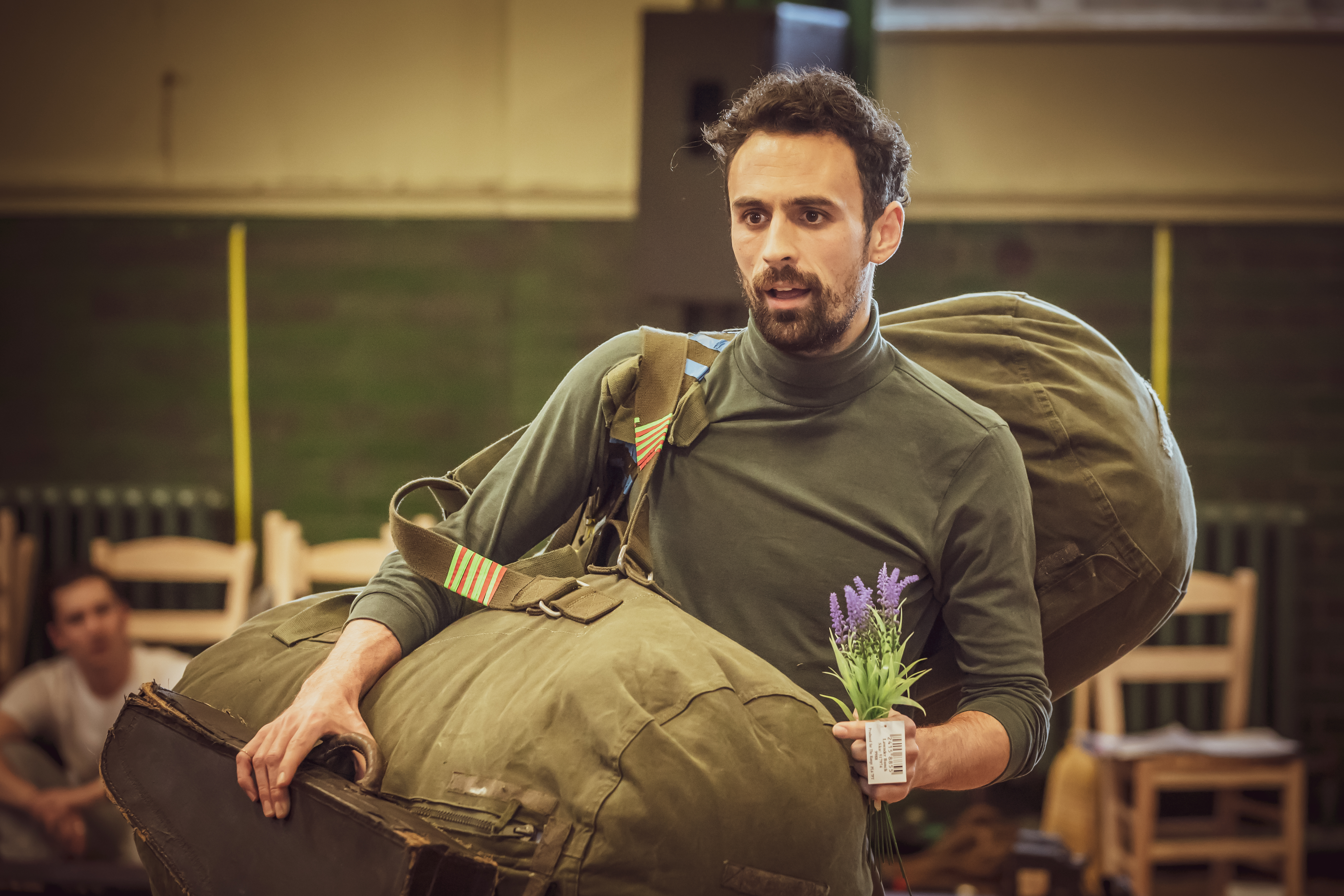 Male sitting down with arms wrapped around an army rucksack whilst starring with surprised facial expression