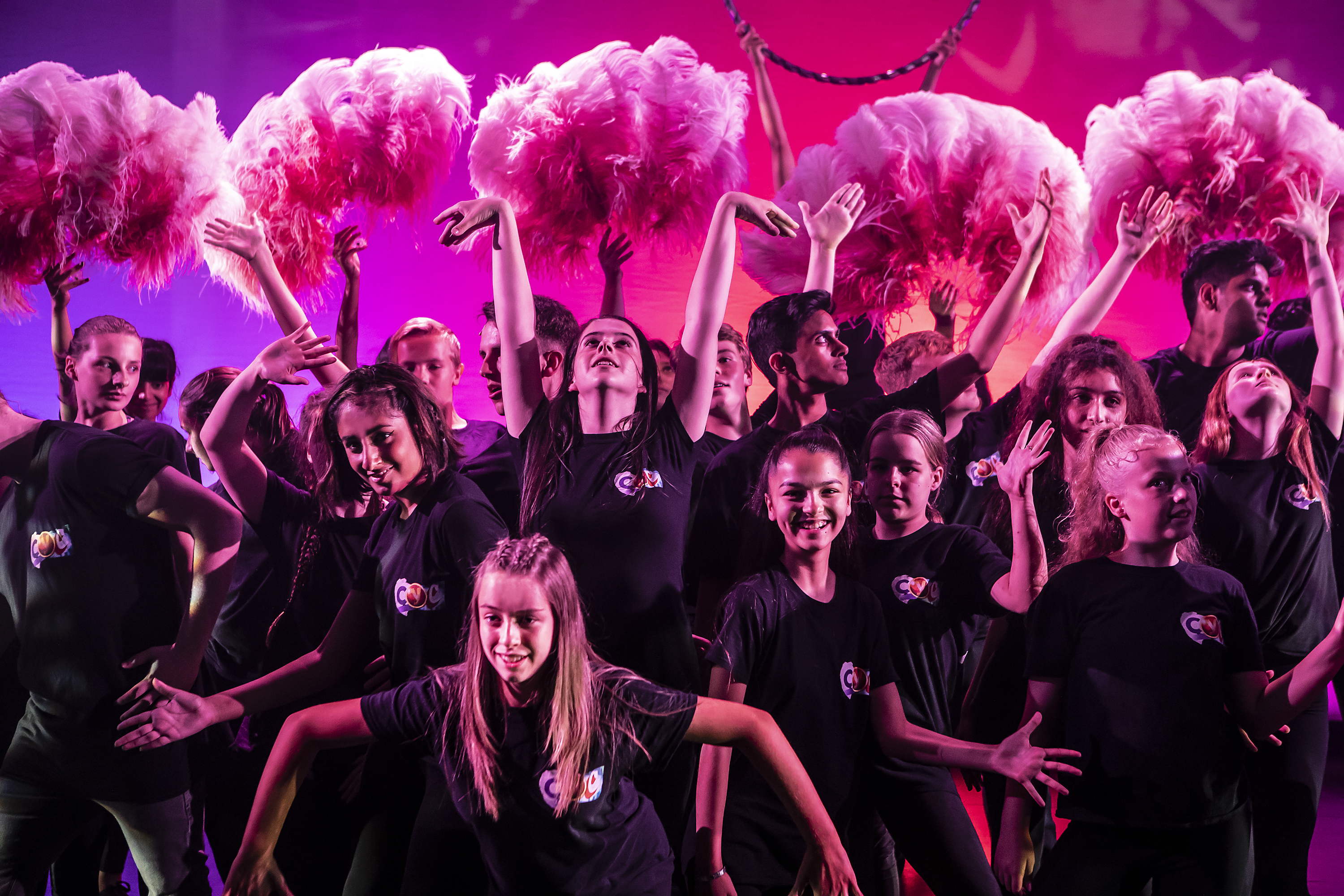 A group of Curve Young Company members hold up pink feathers as part of a dance routine