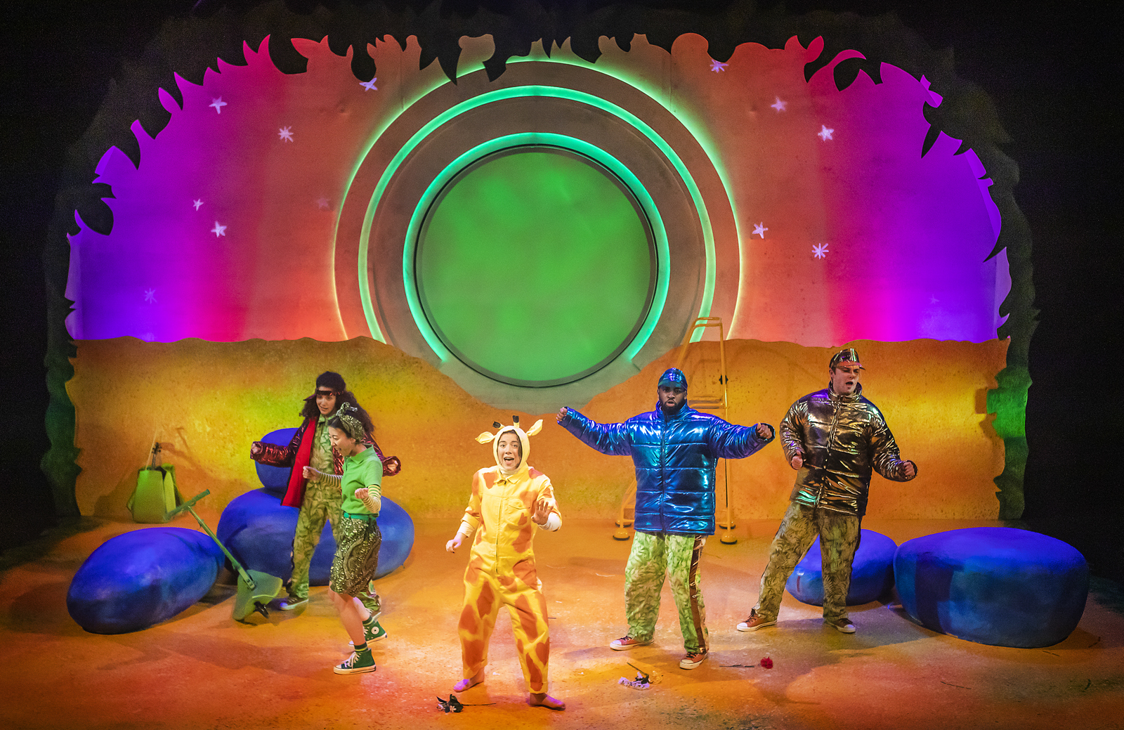 Production image from Giraffes Can't Dance. The Beetles and Cricket dance with Gerald on a yellow-toned set styled as a Savannah at dusk.