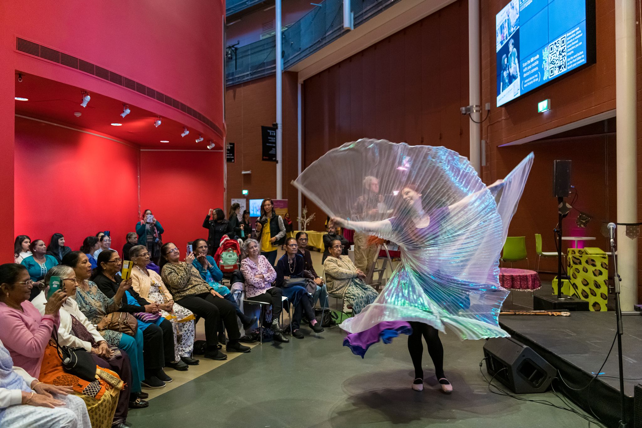 A solo dancer twirls with tulle drapes as an audience watches on.