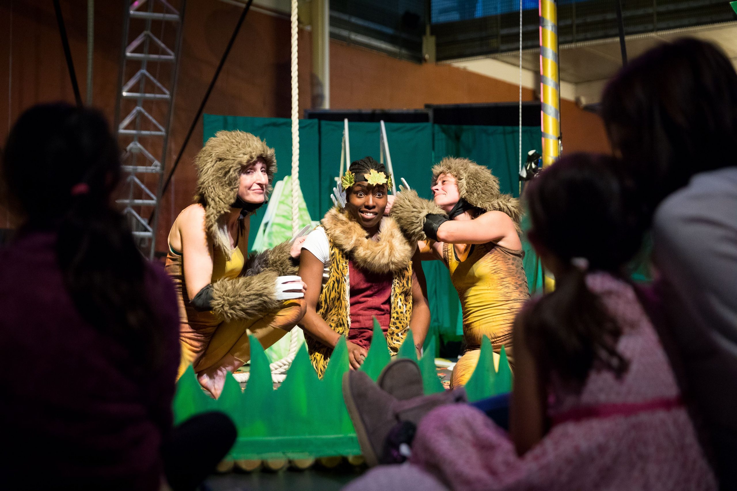 A production image from Tarzanna showing three performers huddled together dressed in animal costumes.