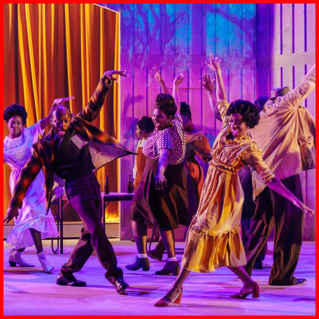 Production image from The Color Purple showing the company dancing together in pairs, in front of a purple and blue toned backdrop with a golden curtain.
