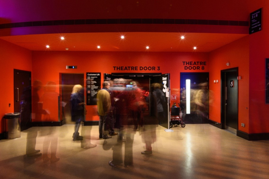 Image of audience member entering through Theatre Door 3, which is set in a red alcove. The public lift is pictured to its left, and stairwell to the right.