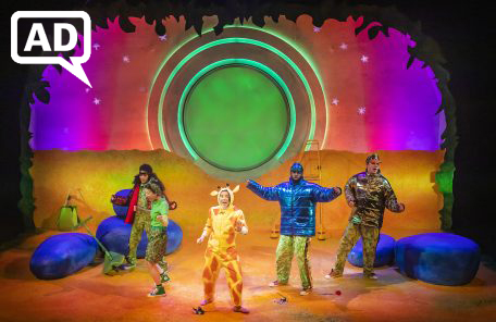 Production image from Giraffes Can't Dance. The Beetles and Cricket dance with Gerald on a yellow-toned set styled as a Savannah at dusk.