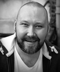 A black and white headshot of Adam Pearce.