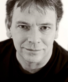 A black and white headshot of Adam Woodyatt