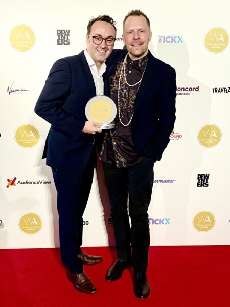 Curve's Chief Executive Chris Stafford and Artistic Director Nikolai Foster at the WhatsOnStage Awards. They smile to the camera as they hold the award on the red carpet.