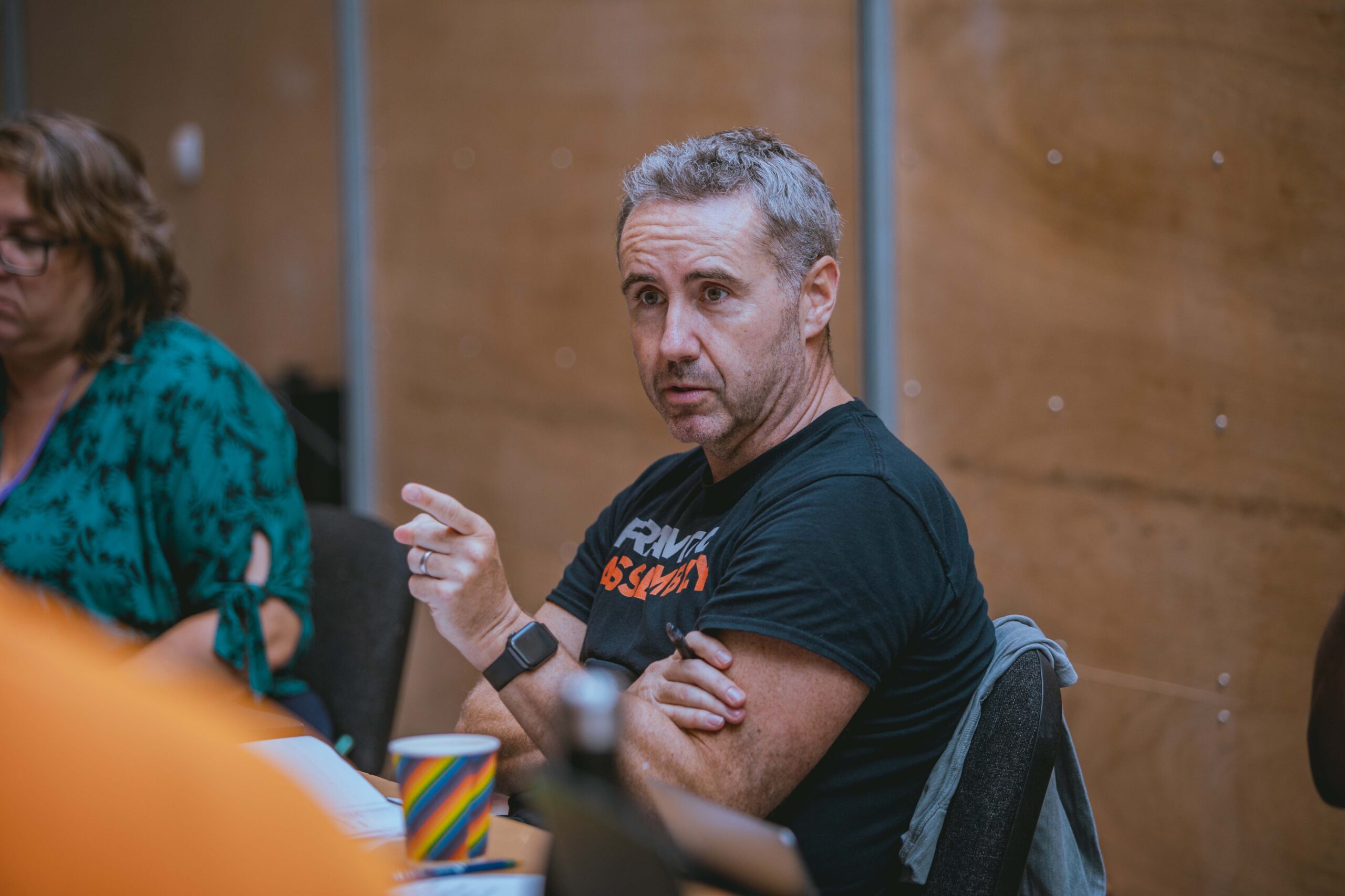 In a wood-cladded rehearsal room, Frantic Assembly Artistic Director Scott Graham is seated, talking to someone in the distance as he points.